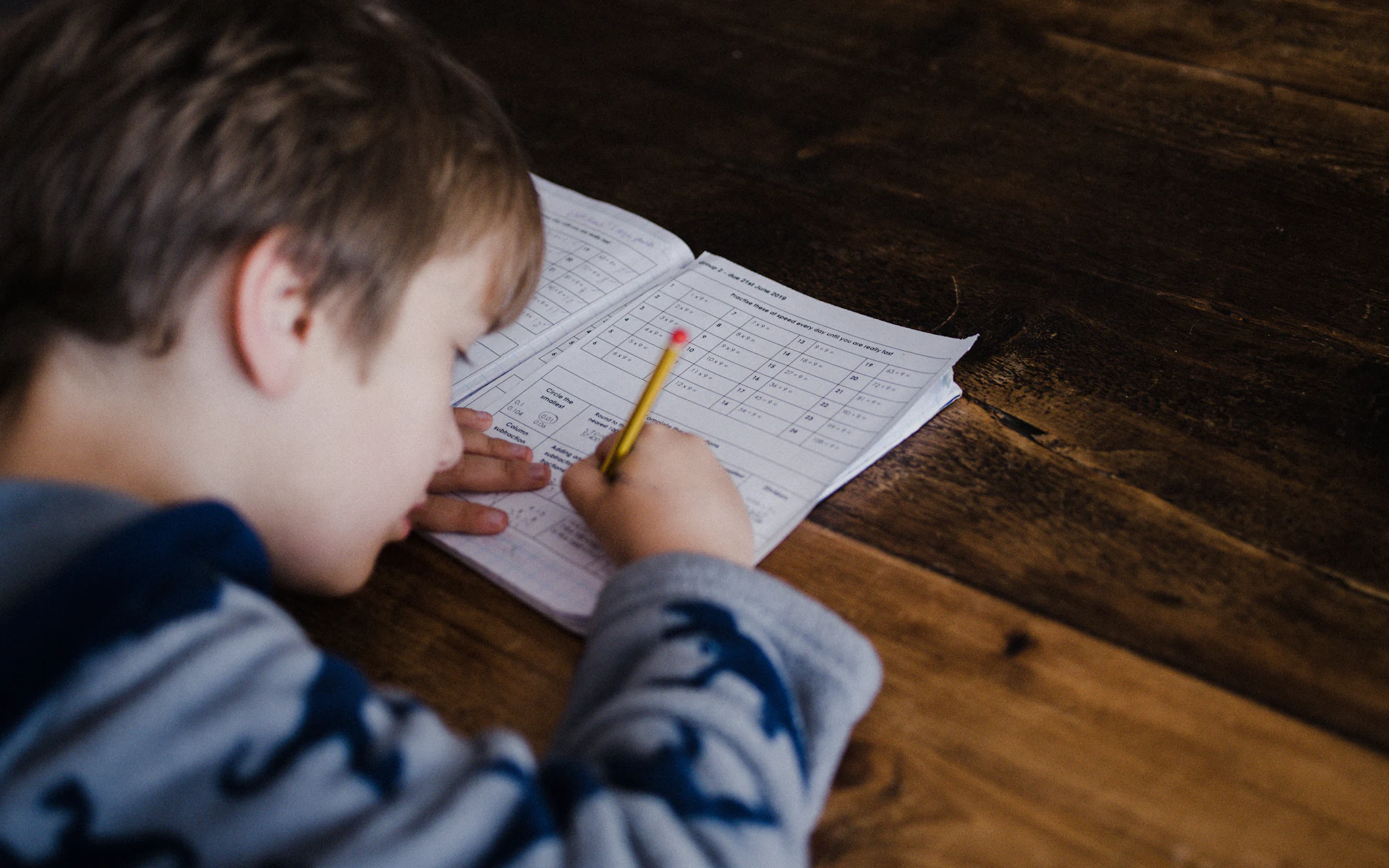 A young student working through a maths worksheet with a pencil